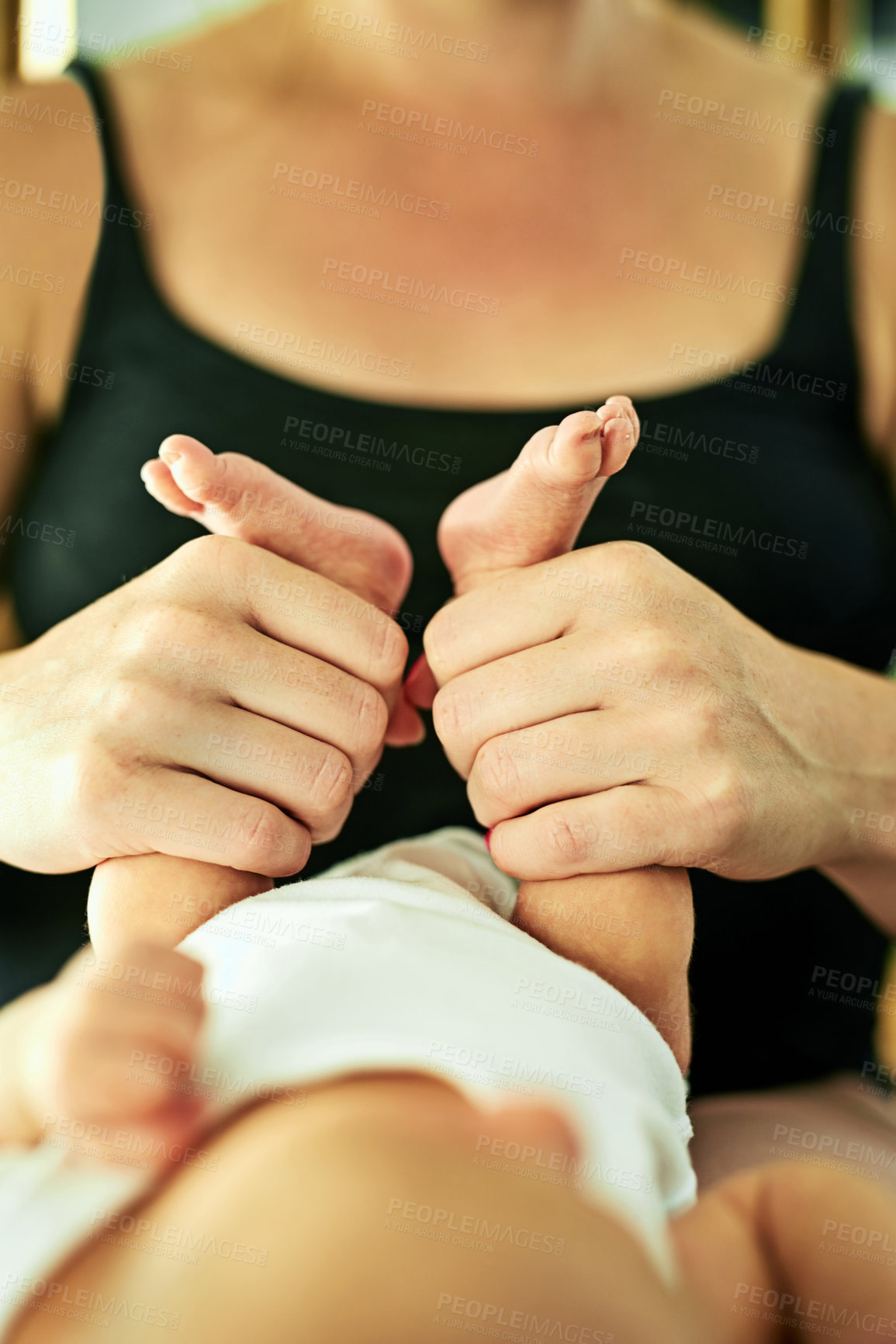 Buy stock photo Shot of a unrecognisable mother holding her little baby boy's legs while he lies comfortably on a bed at home