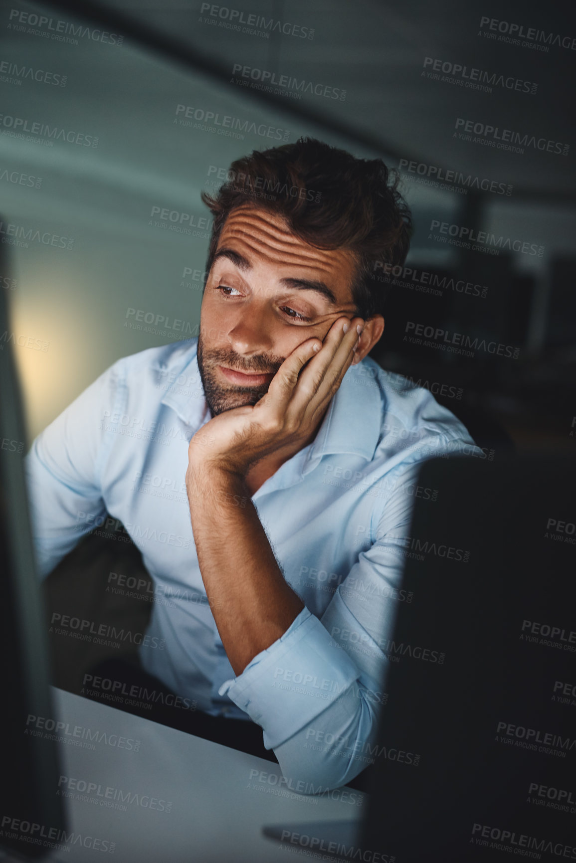 Buy stock photo Shot of a young businessman looking bored while working late in an office
