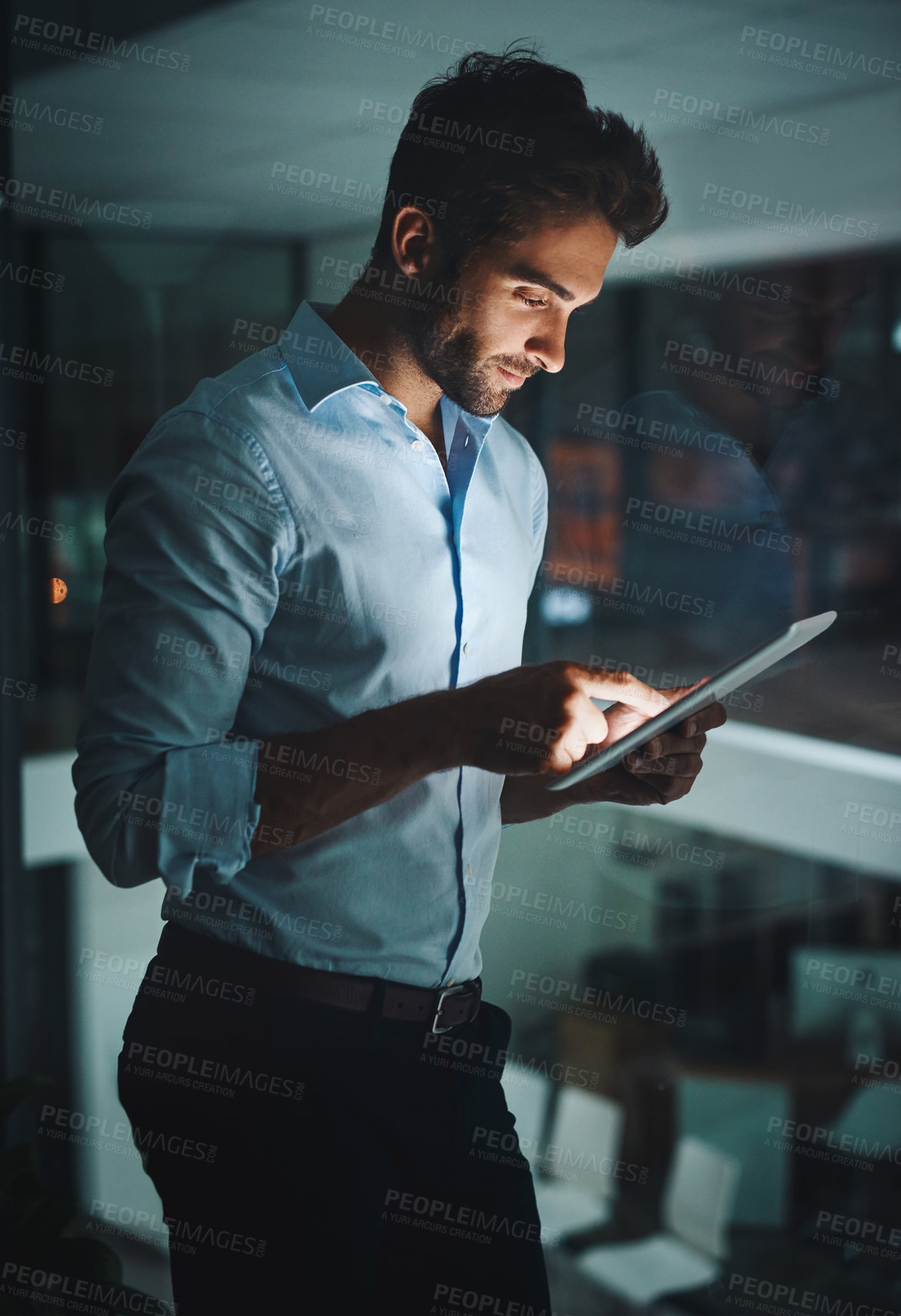 Buy stock photo Shot of a young businessman working late on a digital tablet in an office