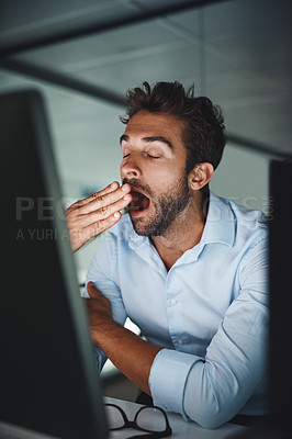 Buy stock photo Shot of a young businessman yawning while working late in an office