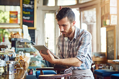 Buy stock photo Shot of a young man using a digital tablet while working in a coffee shop