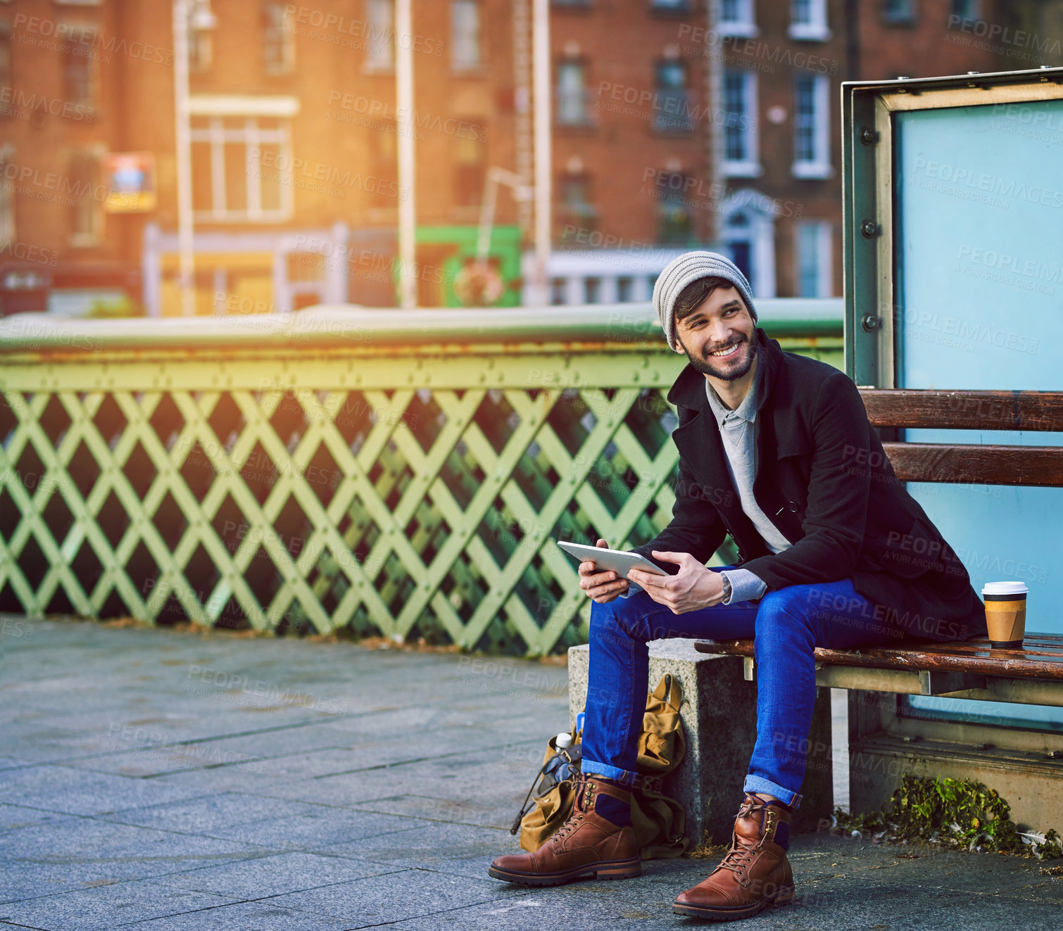 Buy stock photo Man, happy and waiting in city for travel, social media and communication with tablet on holiday. Male person, technology and bus stop in urban town for commute, tourism or web with break on vacation