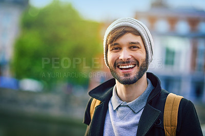 Buy stock photo Man, portrait and smile in city for tourism, sightseeing and travel with blurred background on holiday. Male person, face and commute in urban for adventure, relax and trip with backpack on vacation