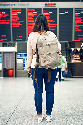 Buy stock photo Rearview shot of an unrecognizable young woman looking at an arrivals and departures board while standing in an airport