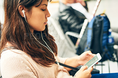 Buy stock photo Cropped shot of an attractive young woman using her smartphone while sitting in a bus station