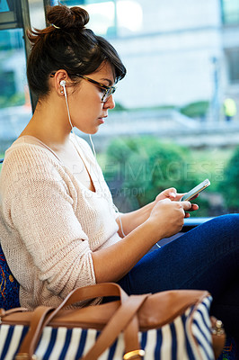 Buy stock photo Cropped shot of an attractive young woman using her smartphone while sitting on a bus