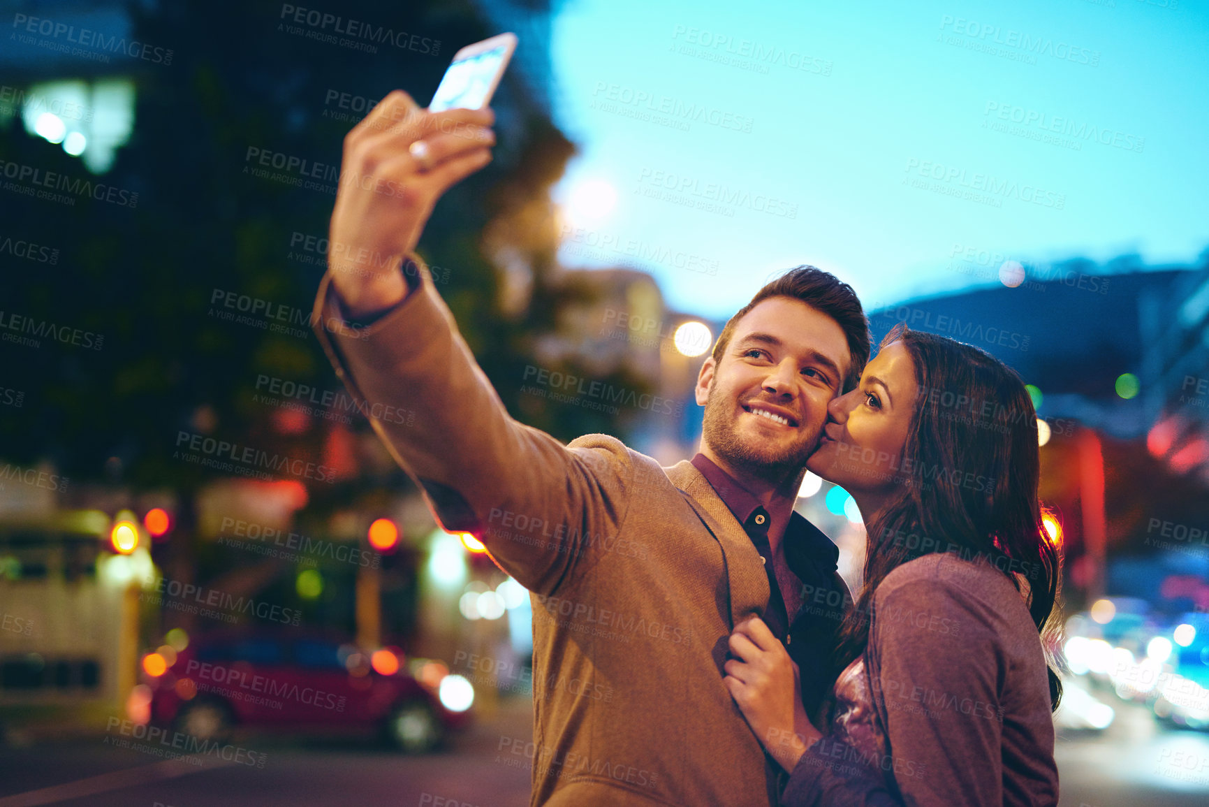 Buy stock photo Cropped shot of an affectionate young couple taking selfies while out on a date in the city