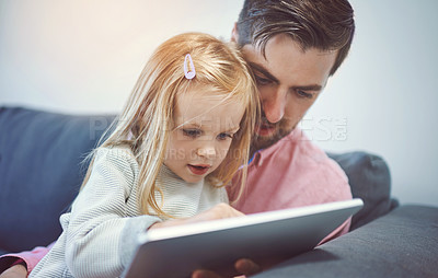 Buy stock photo Shot of an adorable little girl using a digital tablet with her father on the sofa at home