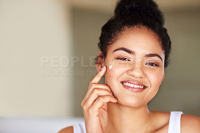 Buy stock photo Portrait of a young woman applying moisturizer to her face