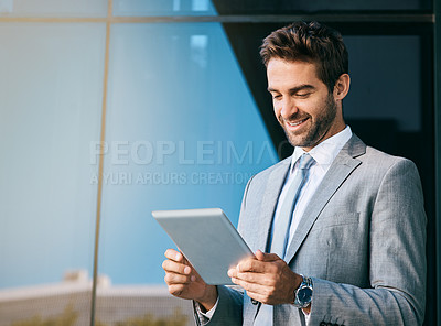 Buy stock photo Shot of a handsome young businessman using a digital tablet outside an office building