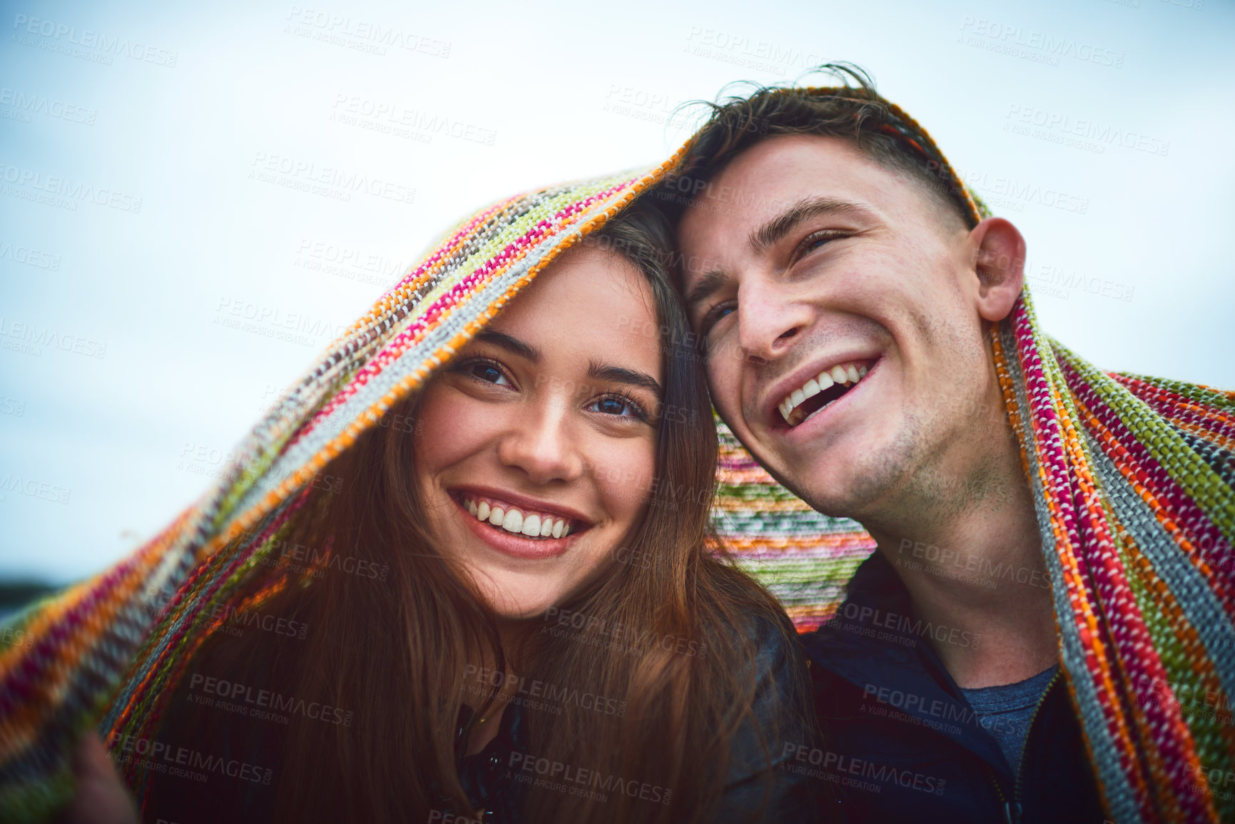 Buy stock photo Shot of a happy young couple covering themselves with a blanket outdoors