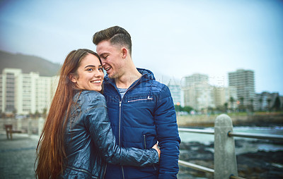 Buy stock photo Couple, hug and outdoor date by the sea with smile, love and ocean with bonding on promenade. Happy, romance and gen z people together with travel and holiday in winter with support and care with fun