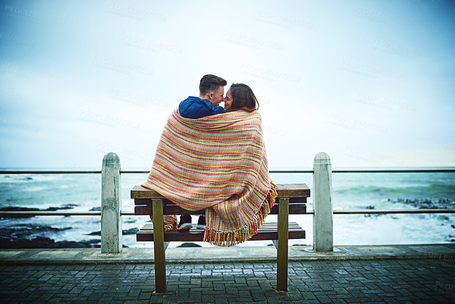 Buy stock photo Couple, beach and blanket with back for love, bonding and relax with relationship, romance and date. Man, woman and ocean for travel, support and connection with partner, cold and weekend together
