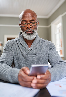 Buy stock photo Cropped shot of a senior man using his cellphone while working on his finances at home