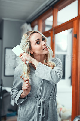 Buy stock photo Shot of a young woman brushing her hair at home
