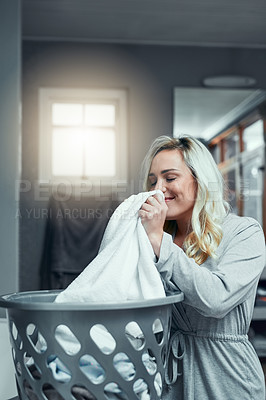 Buy stock photo Shot of a young woman smelling fresh and clean laundry at home