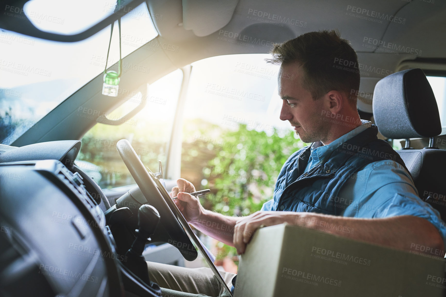 Buy stock photo Shot of a courier writing on a clipboard while sitting in a delivery van