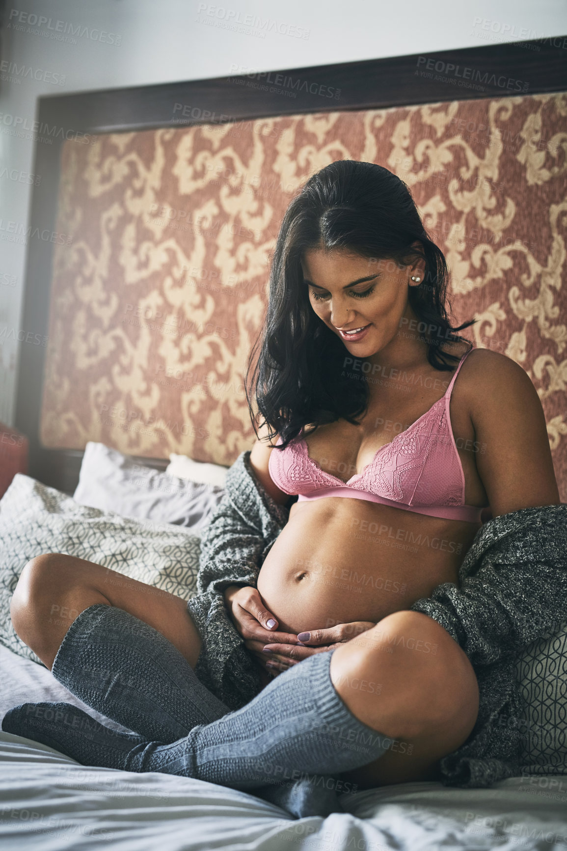 Buy stock photo Full length shot of an attractive young pregnant woman sitting on her bed at home