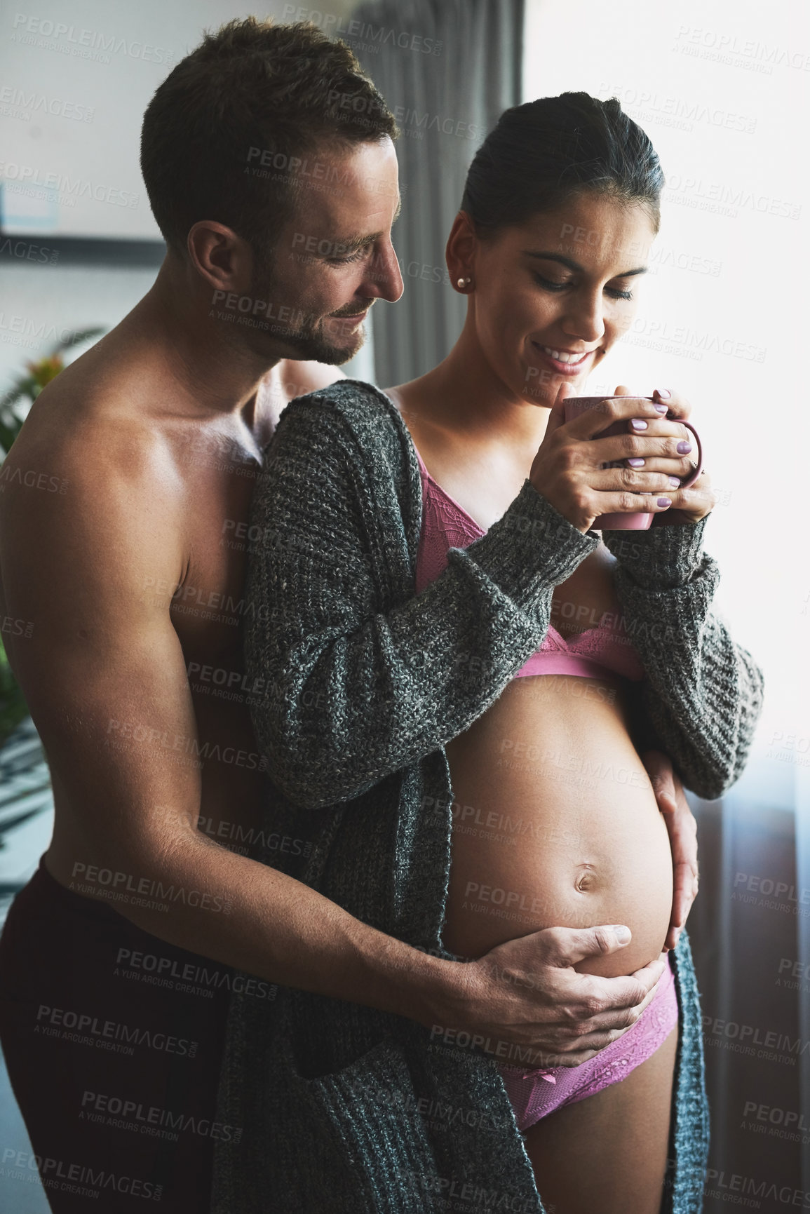 Buy stock photo Pregnancy, couple or hand on stomach at window for love, touch or safety in home. Future parents, pride or woman in underwear for growth, maternity or herbal tea for healing or antioxidants for care