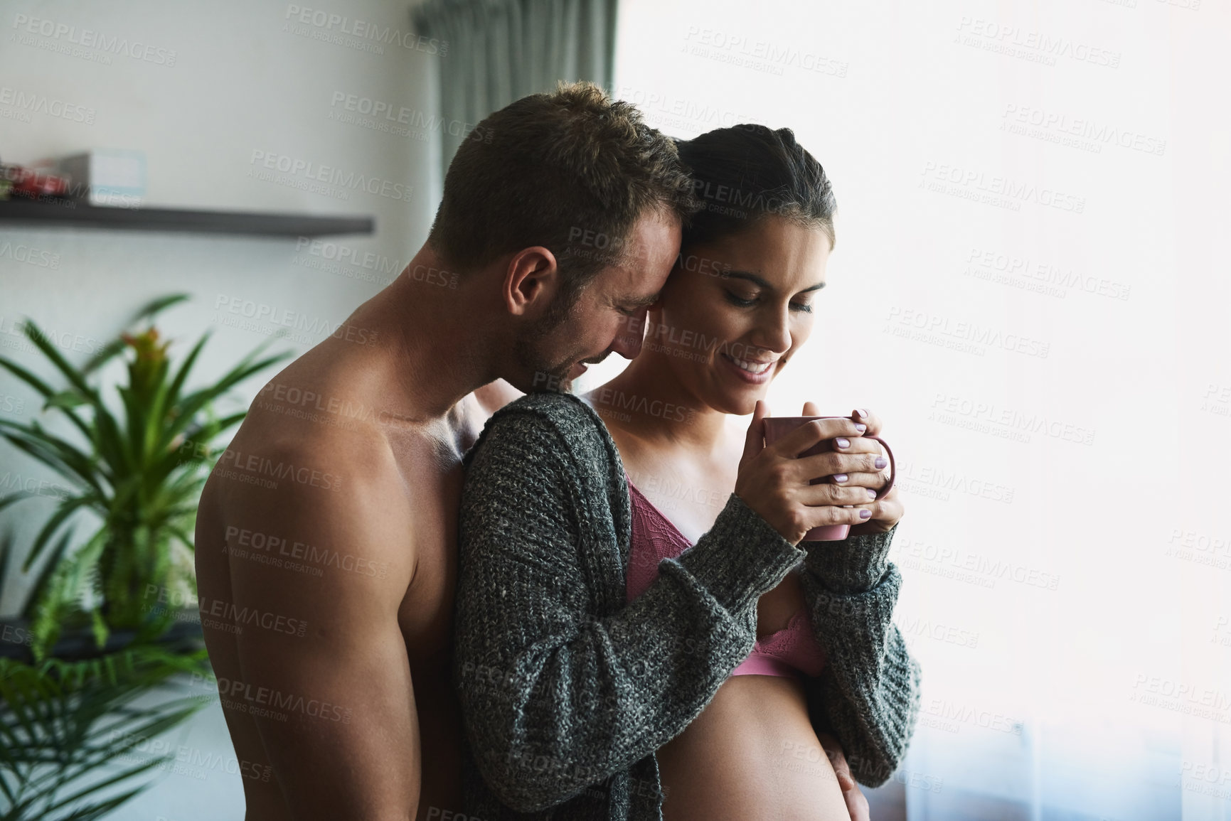 Buy stock photo Pregnancy, couple or hug in home for love, touch or herbal tea for antioxidants at window. Future parents, happy or woman in underwear for growth, maternity or drink for healing with embrace for care