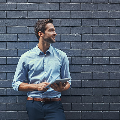 Buy stock photo Shot of a handsome young businessman using a tablet while standing against a grey facebrick wall