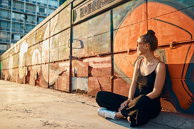 Buy stock photo Full length shot of an attractive young woman sitting against a graffiti wall in the city