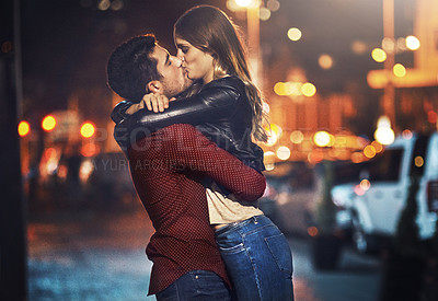 Buy stock photo Shot of a young couple sharing a romantic kiss together outside at night