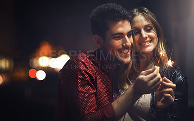 Buy stock photo Shot of a happy young couple celebrating with sparklers outside at night