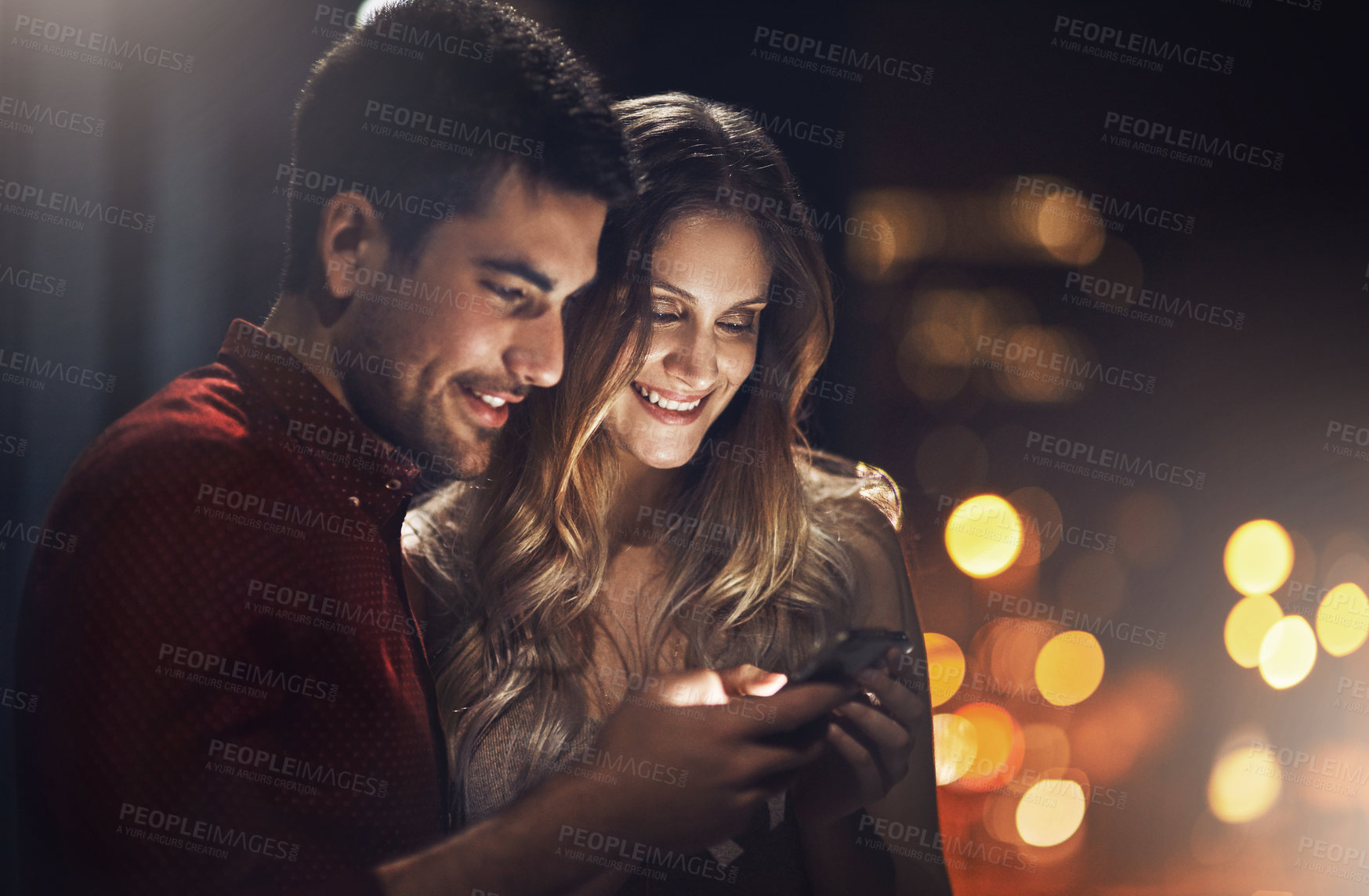 Buy stock photo Shot of a young couple using their smartphones together at night