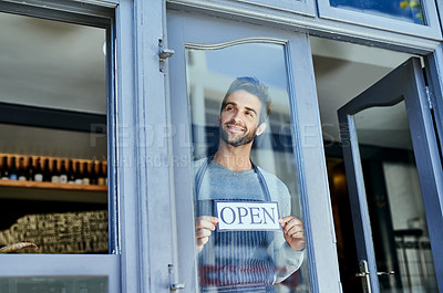 Buy stock photo Shot of a handsome young man hanging an open sign in the window of his business
