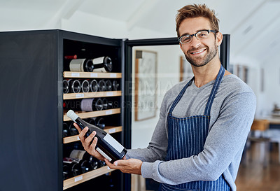 Buy stock photo Bottle, cafe and portrait of sommelier man at wine shelf for selection, choice and hospitality. Smile, alcohol and restaurant server, waiter or small business owner with drinks for service quality