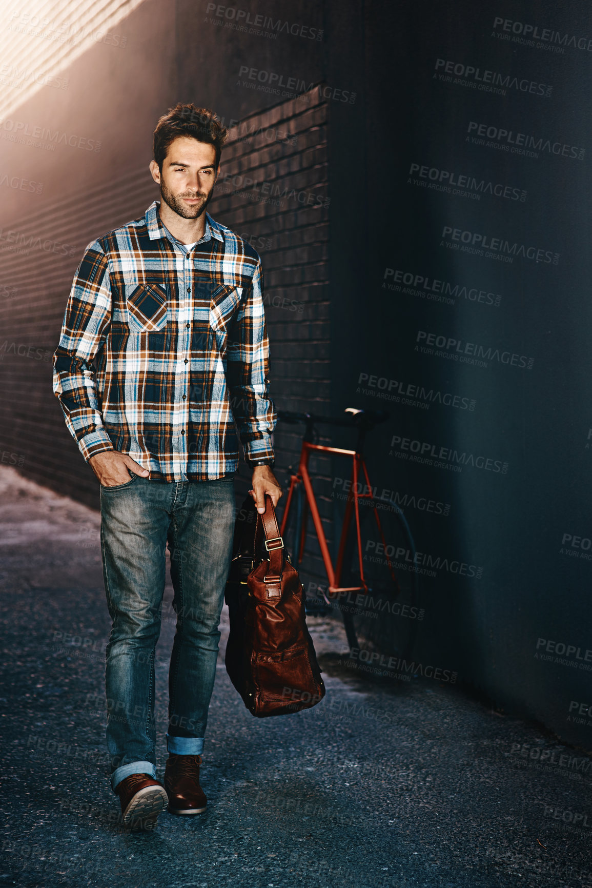 Buy stock photo Shot of a handsome young man carrying a bag and walking down a city street