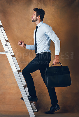 Buy stock photo Studio shot of a handsome young businessman climbing a ladder against a brown background