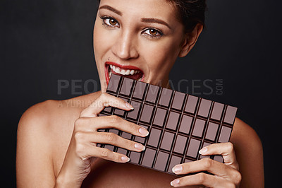 Buy stock photo Studio shot of an attractive young woman biting into a slab of chocolate