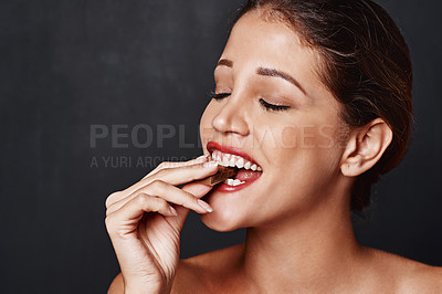 Buy stock photo Studio shot of an attractive young woman biting into a piece of chocolate