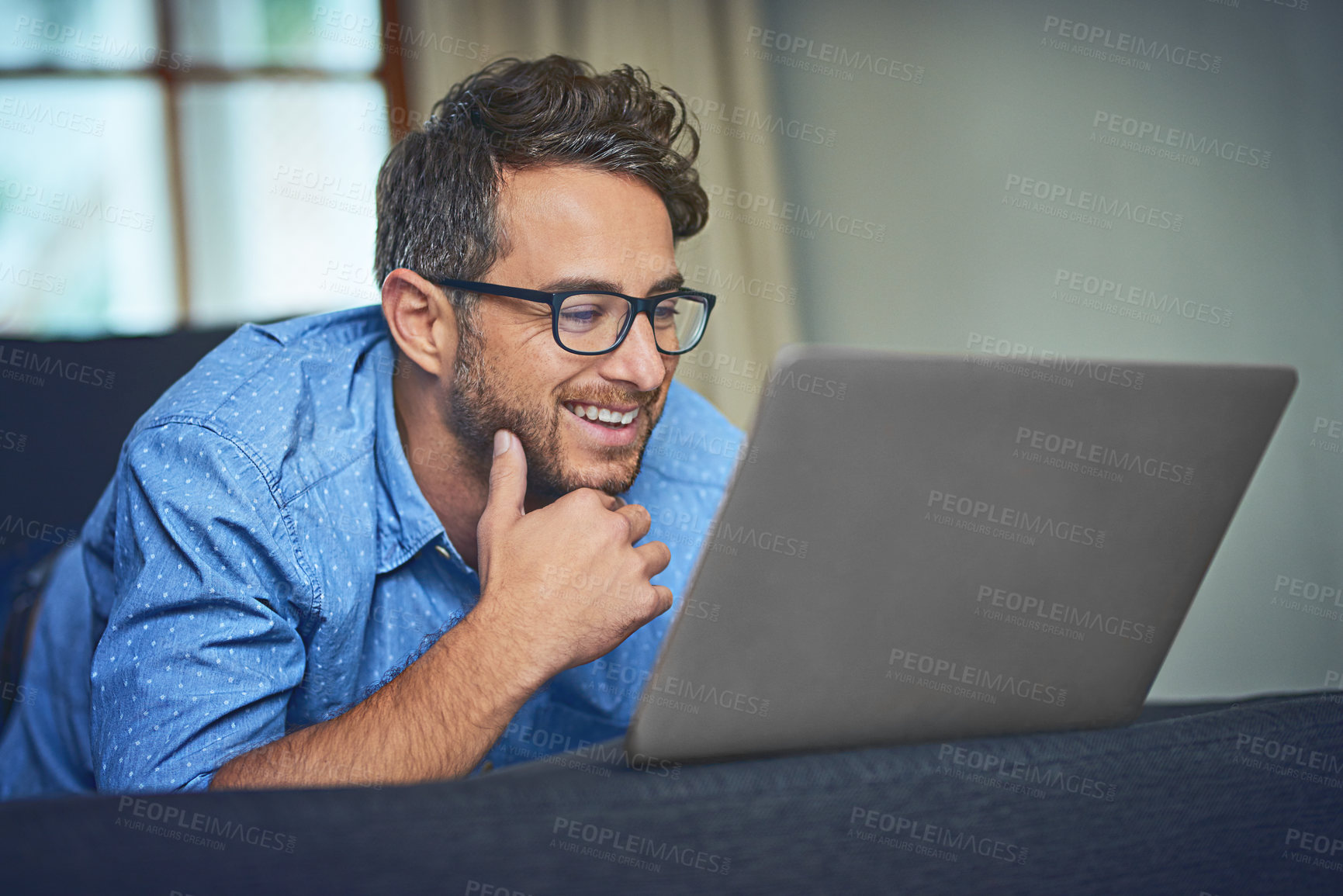 Buy stock photo Shot of a young man using a laptop on the sofa at home