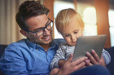 Buy stock photo Shot of a father and son using a digital tablet together on the sofa at home
