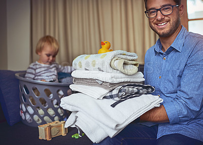 Buy stock photo Portrait of a young man holding a load clean laundry with his son in the background