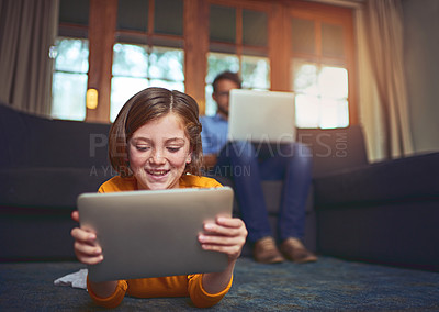 Buy stock photo Shot of a little girl using a digital tablet on the floor at home with her father in the background