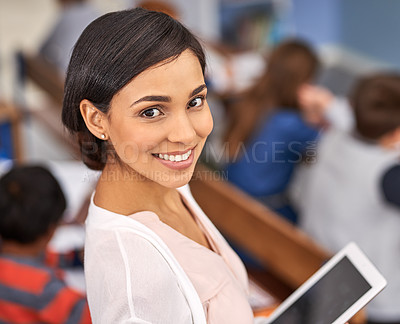 Buy stock photo Portrait of a happy young teacher holding a tablet with her students in the background
