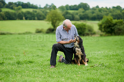 Buy stock photo Shot of a cheerful mature farmer kneeling and holding his pet dog outside on a green field