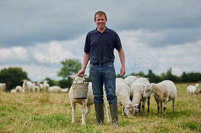 Buy stock photo Portrait of a cheerful young farmer walking with a herd of sheep and feeding them while holding a bucket