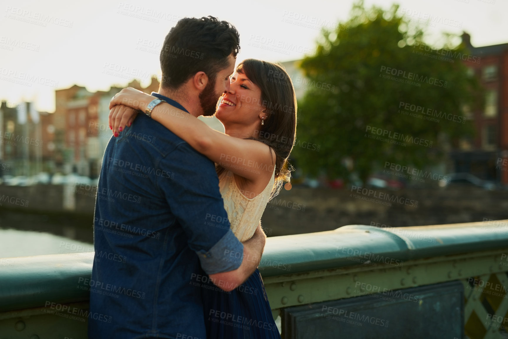 Buy stock photo Happy, couple and hug with love in city for romantic outdoor date, weekend and vacation together. Man, woman and kiss in romance with connection at sunset for holiday adventure, marriage and embrace