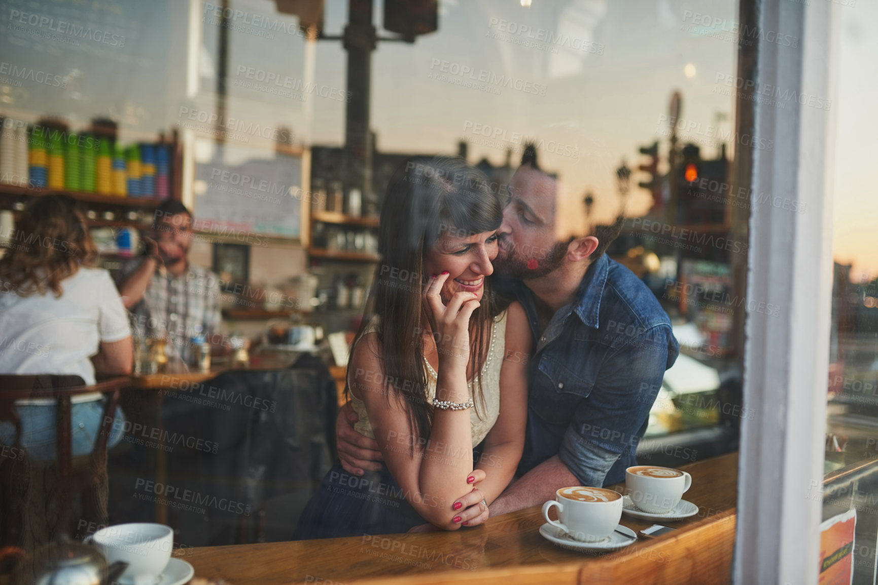 Buy stock photo Cropped shot of a handsome young man kissing his girlfriend on the cheek while sitting in a coffee shop during a date