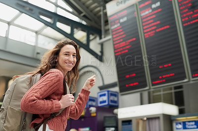 Buy stock photo Low angle portrait of an attractive young woman pointing at a flight information display in an airport