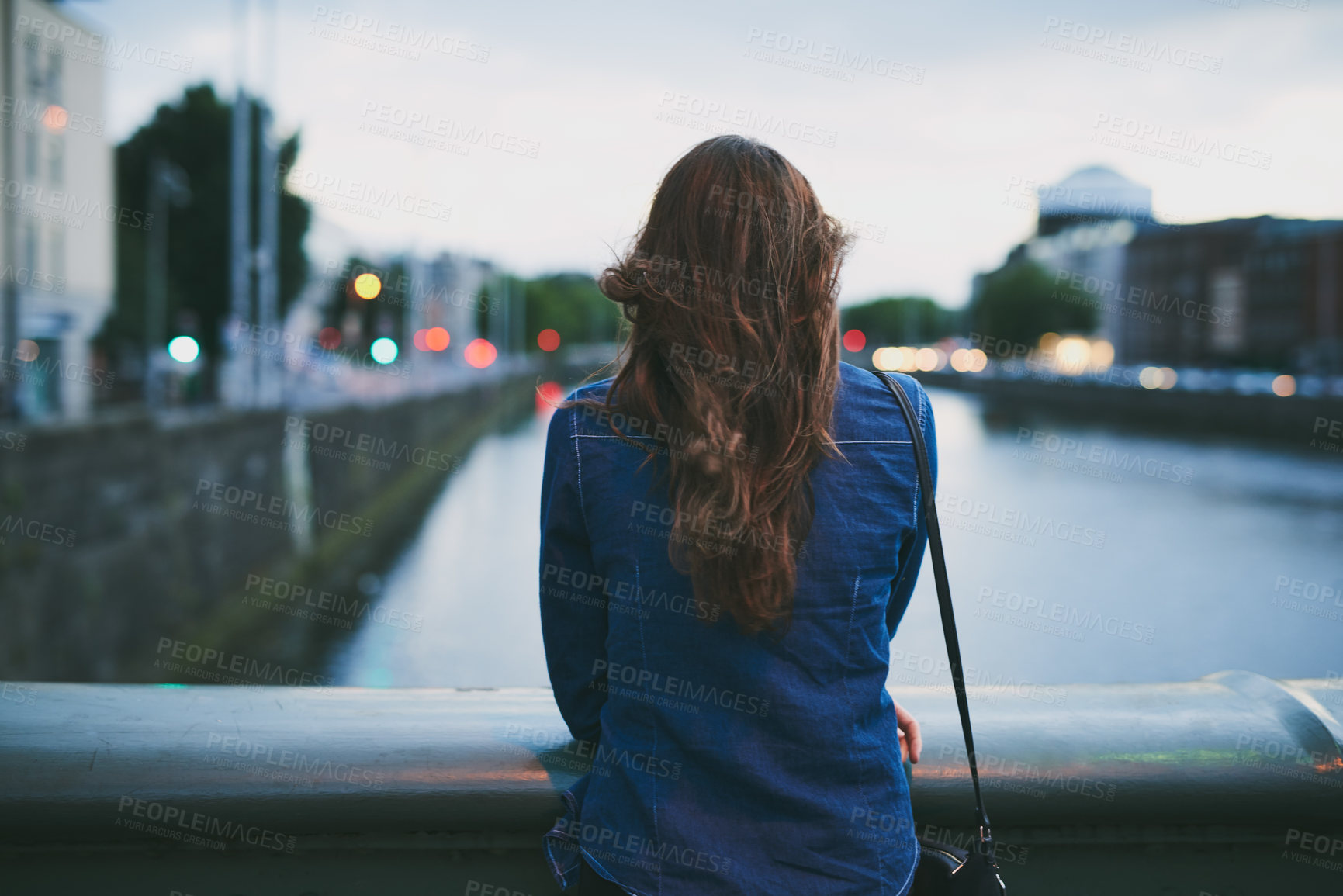 Buy stock photo Rearview shot of an unrecognizable young woman taking in the city views while standing on a bridge