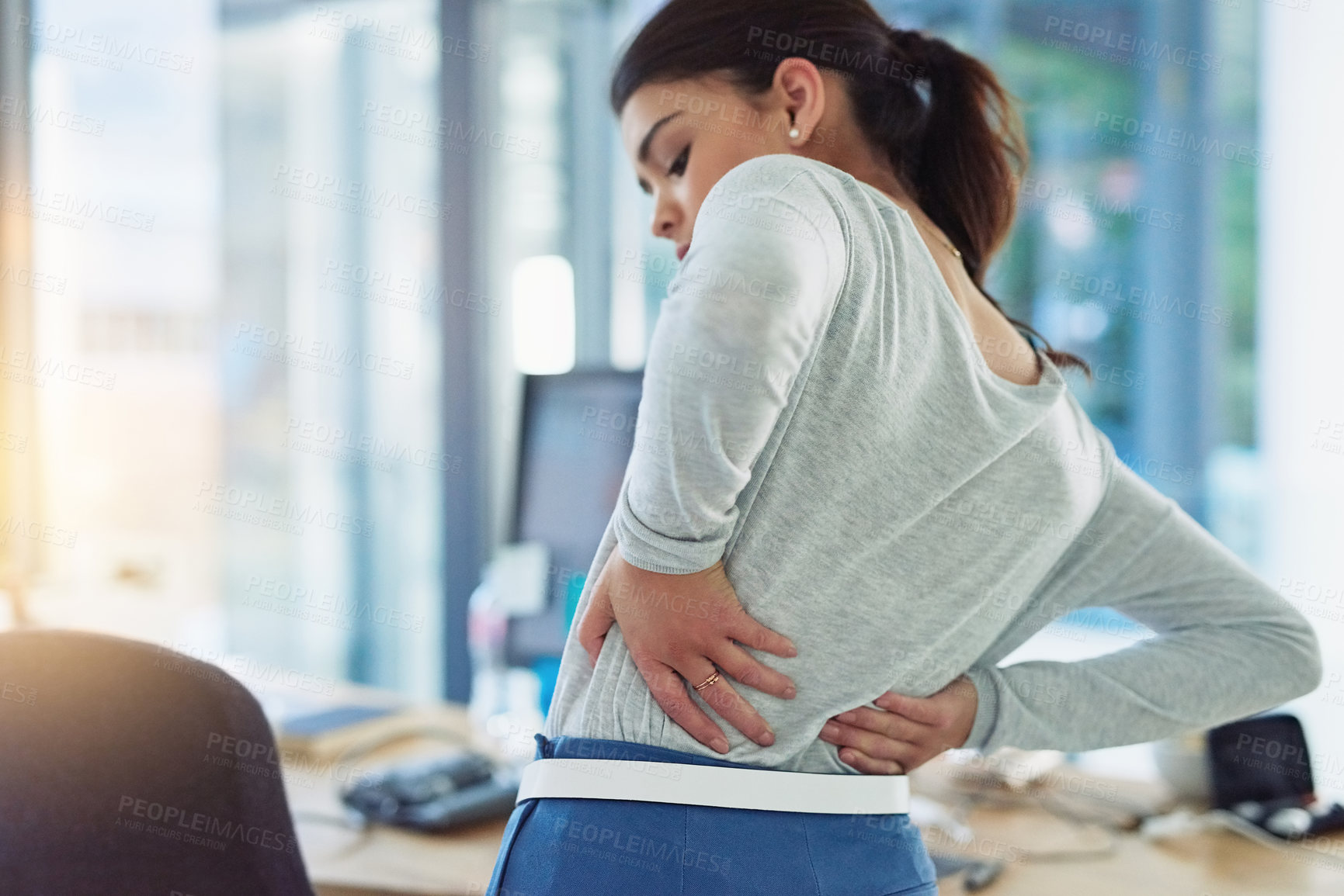 Buy stock photo Shot of a young businesswoman suffering from back pain while working in an office