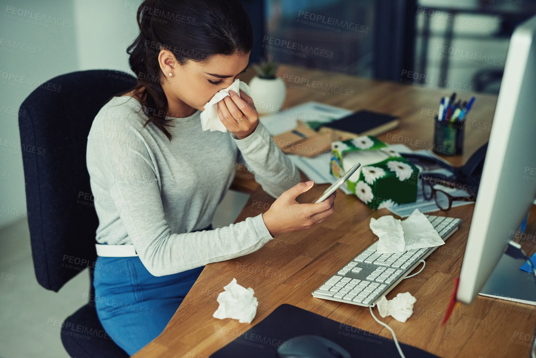 Buy stock photo Blowing nose, phone and a business woman working at her desk in the office while sick, ill or unwell. Covid, tissue and allergies with a young female employee typing a mobile text message at work