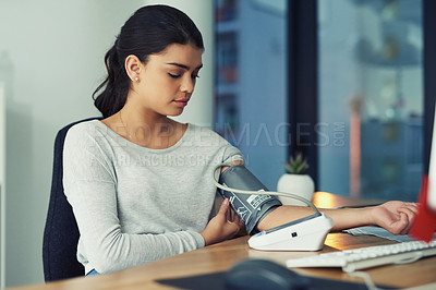 Buy stock photo Shot of a young businesswoman checking her blood pressure in an office
