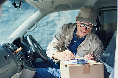Buy stock photo Shot of a courier writing on a clipboard while sitting in a delivery van